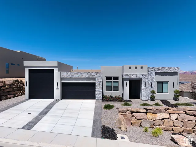 Contemporary exterior featuring a smooth stucco finish, stone veneer accents, a three-car garage with black doors, and a decorative stacked-stone retaining wall