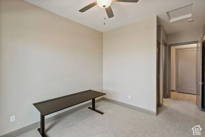 Neutral-toned interior space featuring light-colored wall-to-wall carpeting, a ceiling-mounted light fixture with an integrated fan, and a solid-core interior door