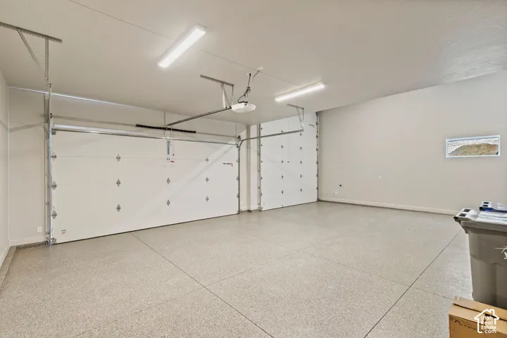 Spacious three-car garage featuring epoxy-coated flooring, dual sectional doors, and integrated overhead fluorescent lighting