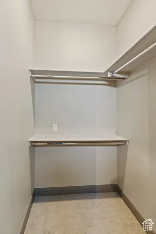Storage closet featuring dual-level shelving, integrated metal clothing rods, and wall-mounted electrical outlet