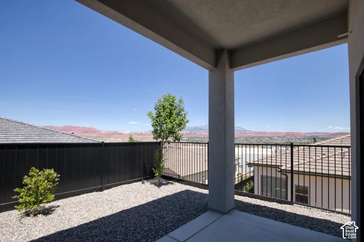 Covered concrete patio with a structural pillar, black metal perimeter fencing, and desert-inspired landscape rock featuring mature shrubbery