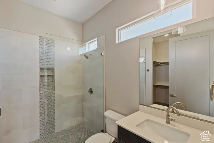Bathroom featuring a walk-in shower with glass enclosure, decorative vertical tile accent, built-in recessed shelving, vanity with quartz countertop, and horizontal clerestory window