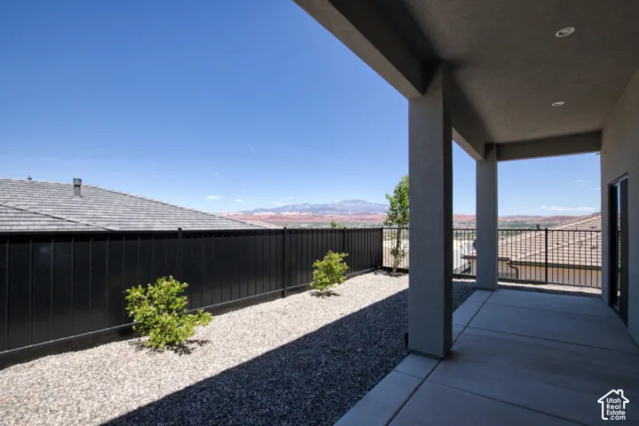 Covered concrete patio featuring recessed lighting, metal privacy fencing, gravel landscaping, and mountain backdrop