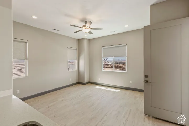 Neutral-toned interior featuring wood-finish flooring, recessed lighting, a central ceiling fan, and multi-pane windows with roller shades