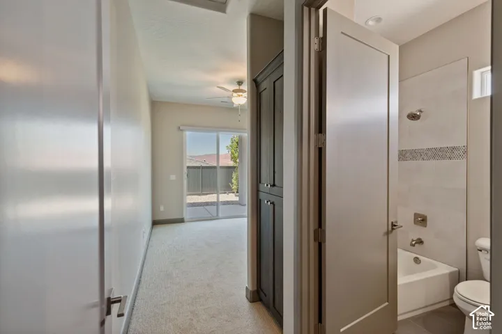 Full-height dark wood-finish cabinetry, sliding glass door with external patio access, ceiling fan, and bathroom featuring tile-surround tub with decorative inlay