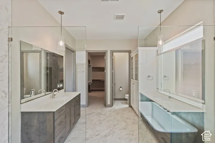 Dual vanities featuring dark cabinetry, solid-surface countertops, undermount sinks, and wall-mounted pendant lighting