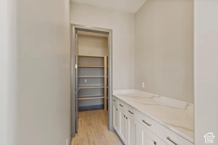 Butler pantry featuring white cabinetry with neutral stone-finish countertops, wood-finish flooring, and a walk-in storage area with integrated shelving