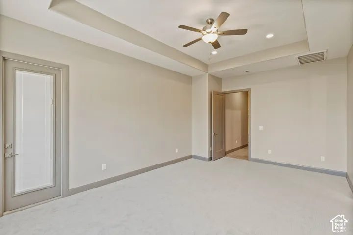 Tray ceiling, neutral carpeting, ceiling fan with integrated lighting, recessed lighting, and a single-light door