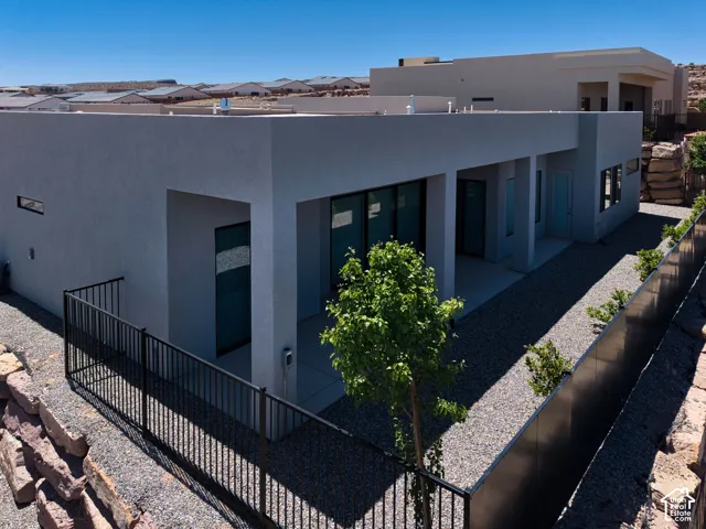 Contemporary exterior featuring a stucco facade, expansive covered patio, black metal fencing, and tiered stone retaining walls