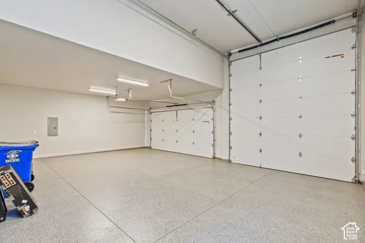 High-ceiling garage featuring epoxy-coated flooring, two overhead roll-up doors, and integrated fluorescent lighting