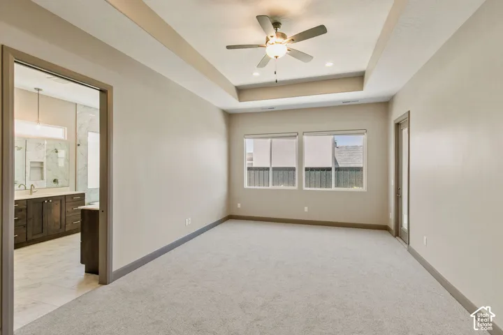 Room featuring a tray ceiling with a central fan, neutral carpeting, and dual-pane windows