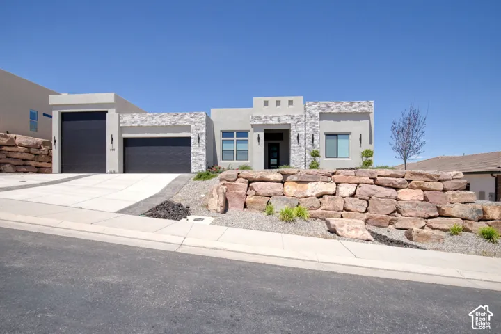 Contemporary exterior featuring smooth stucco finish, stacked stone veneer accents, multi-car garage with dark-toned doors, and decorative boulder retaining walls
