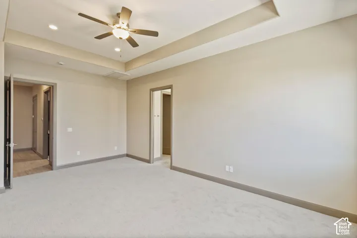 Neutral-toned room featuring a tray ceiling, recessed lighting, wall-to-wall carpeting, and an integrated ceiling fan with light fixture