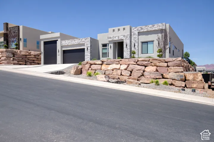Contemporary exterior featuring a stucco facade with stacked stone masonry accents, large-format boulder retaining walls, and multi-car garage with dark-finish doors
