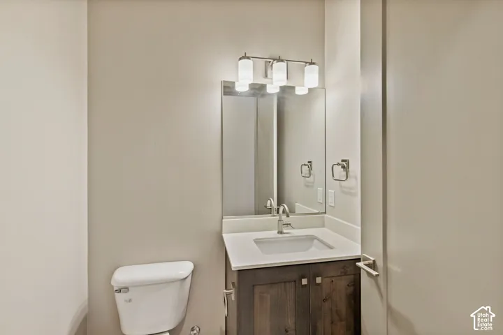 Vanity featuring a stained wood cabinet, solid-surface countertop, and integrated sink with a polished chrome faucet, accented by a three-light vanity fixture and a frameless mirror
