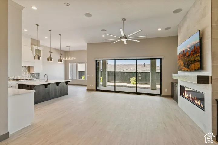 Open-concept living space featuring wood-finish flooring, a linear gas fireplace with a stone-surround wall, a center island with pendant lighting, and multi-panel sliding glass doors