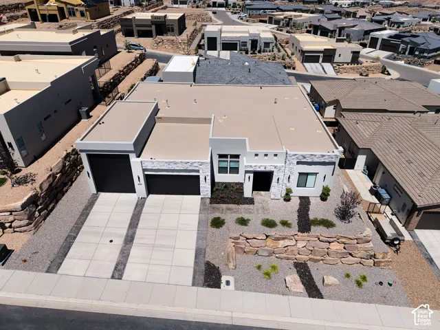 Single-story residence featuring a contemporary exterior, textured stone accents, a three-car garage, concrete driveway, and a tiered rock retaining wall