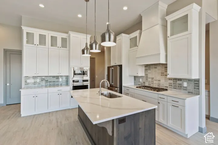 Kitchen featuring white shaker-style cabinetry with glass-front uppers, quartz countertops, a stone tile backsplash, a central island with dark wood-finish cabinetry, and stainless steel appliances including a built-in oven and gas cooktop