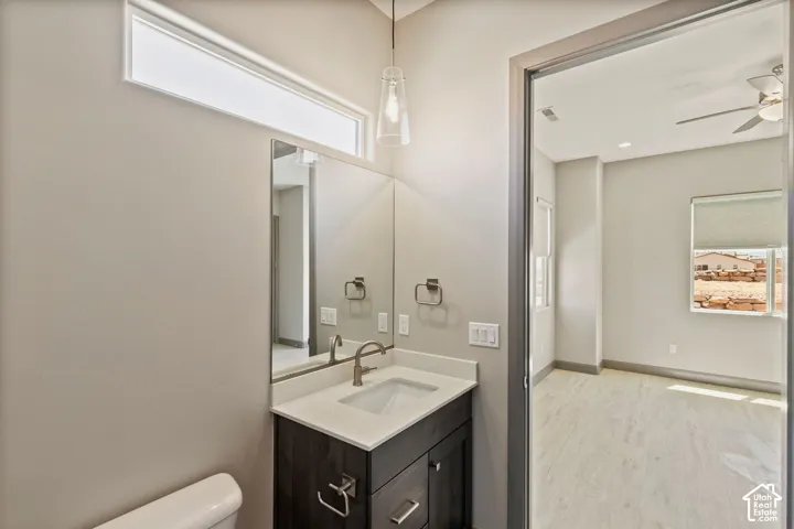 Bathroom featuring a dark wood-finish vanity, light-toned countertop with an integrated rectangular sink, wall-mounted mirror, pendant lighting, and transom window