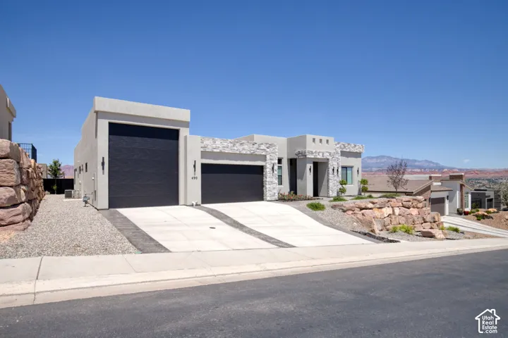 Contemporary exterior featuring stucco siding with stacked stone accents, two-car and RV garage bays, concrete driveway, and natural rock retaining walls