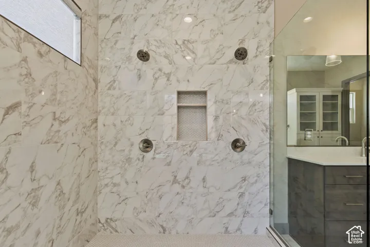 Walk-in shower featuring floor-to-ceiling stone-patterned wall tile, multiple shower heads, a built-in recessed niche, and a glass enclosure