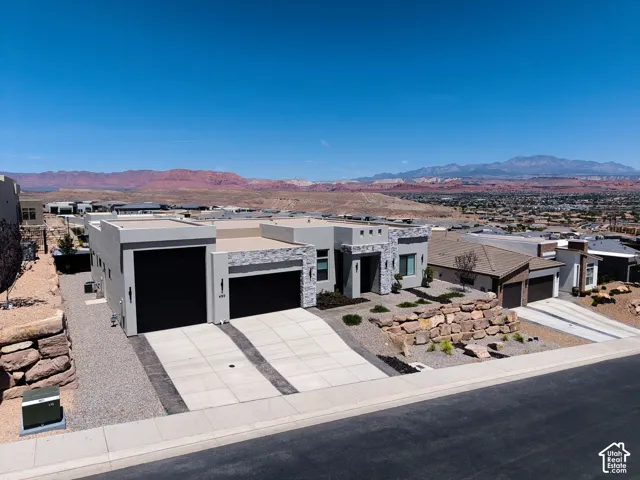 Modern desert-style exterior featuring stone veneer accents, flat roofline, two-car garage with black doors, concrete driveway, and mountain backdrop
