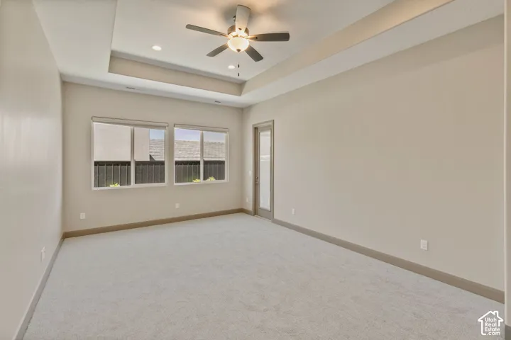 Tray ceiling with integrated recessed lighting, central ceiling fan, carpeted flooring, and dual-pane windows
