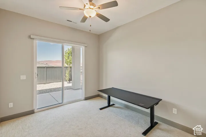 Neutral-toned interior space featuring sliding glass doors, neutral carpeting, and a ceiling-mounted fan with integrated lighting