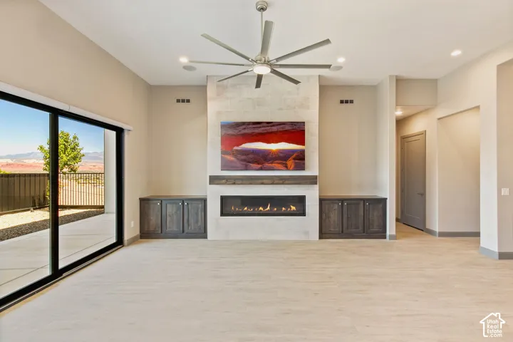 Living area featuring light-toned flooring, a linear fireplace with a stone surround, a stained wood mantel, and custom built-in cabinetry