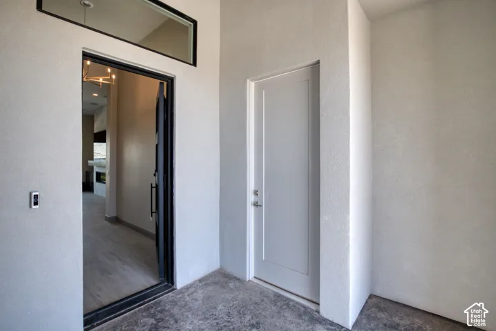 Covered entry featuring a dark-framed glass door, transom window, solid-panel secondary door, and concrete flooring