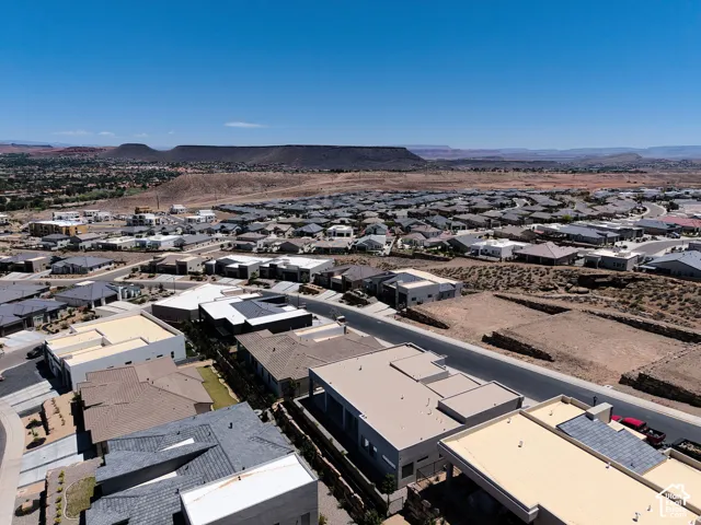 Aerial perspective of residential community featuring flat-roof architectural profiles, paved streets, and expansive desert landscape with mountain silhouettes