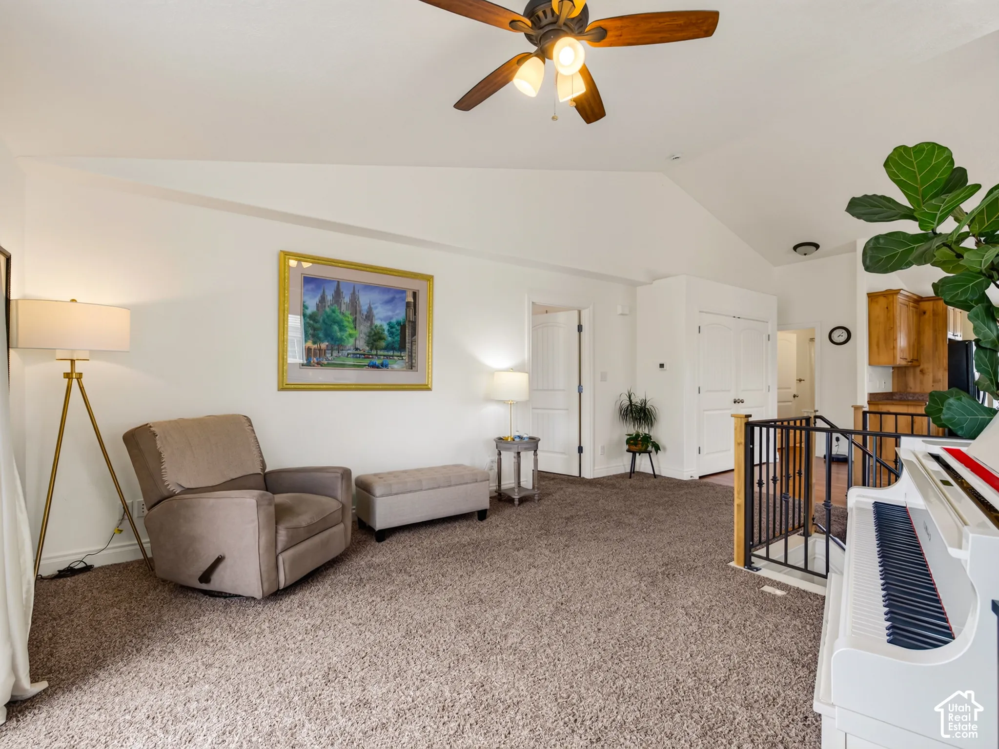Vaulted ceilings featuring a central ceiling fan with integrated lighting, wall-to-wall carpeting, and a black metal handrail with wood accents
