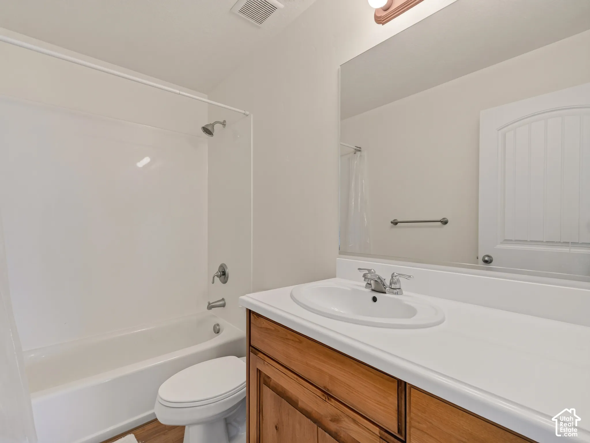 Bathroom featuring a wood-finish vanity with a white countertop and oval undermount sink, a full-width wall mirror, and a tub-shower combination with white surround