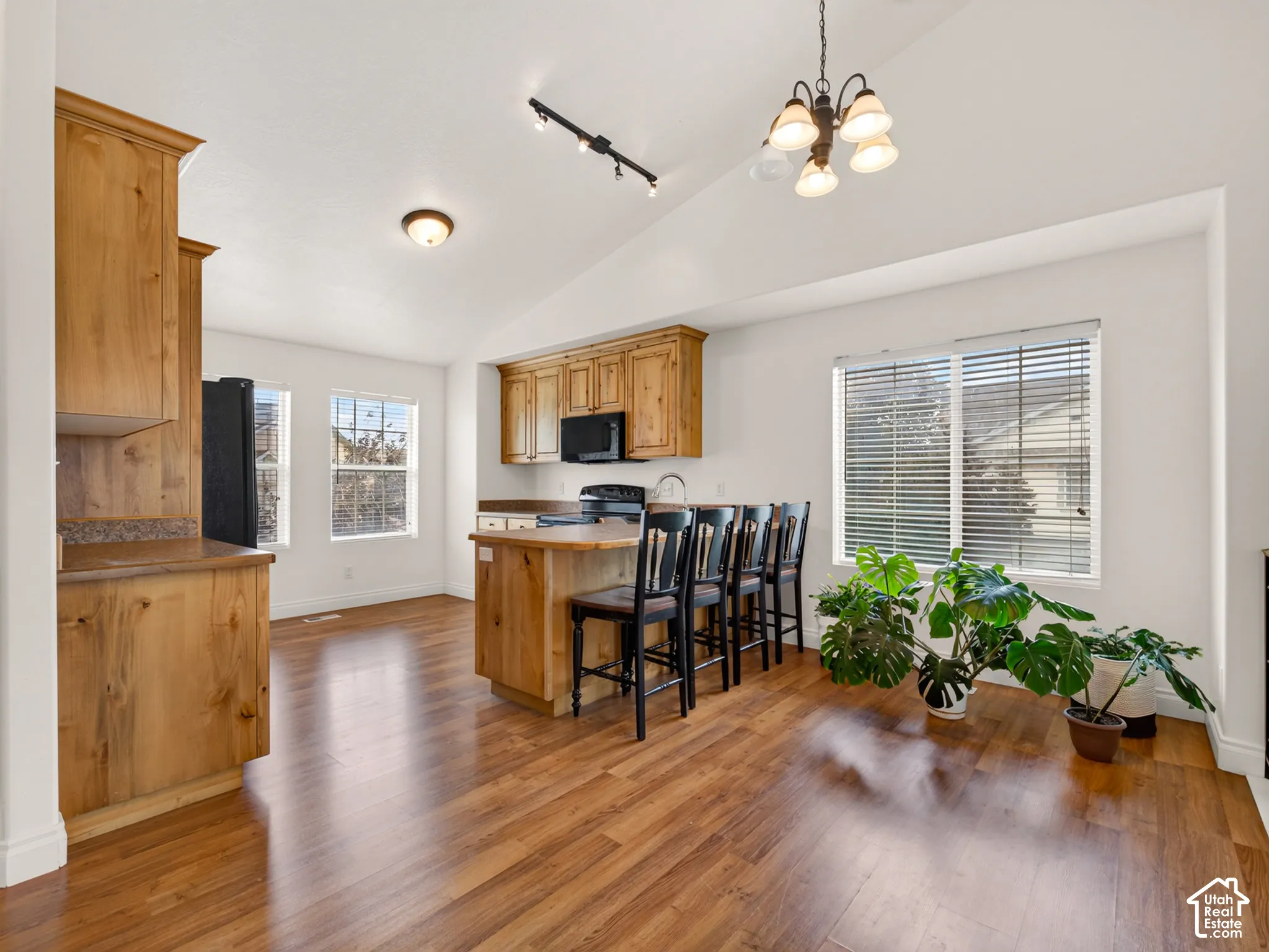 Kitchen featuring wood-finish cabinetry, a central island with integrated seating, vaulted ceilings, and wood-finish flooring