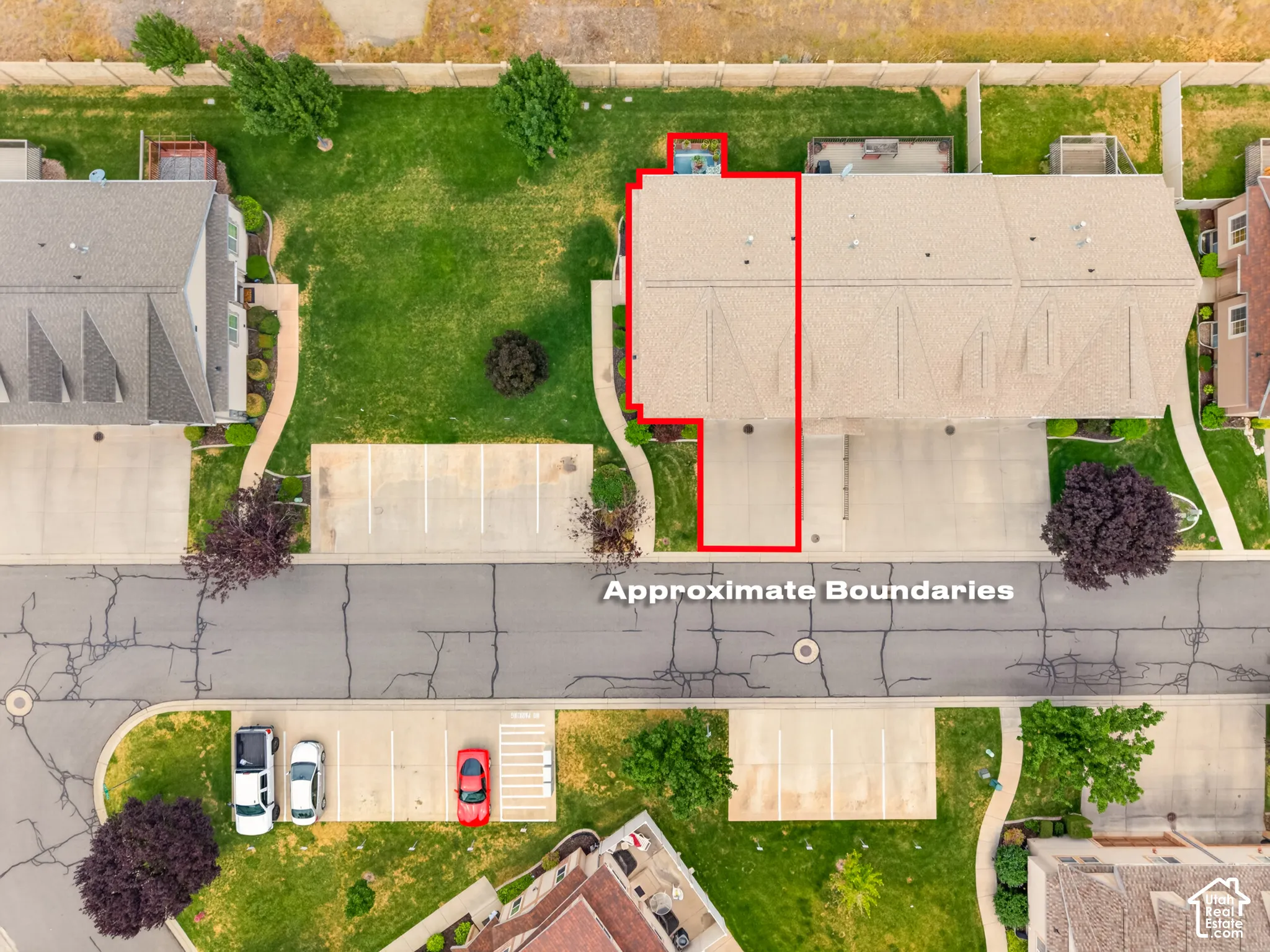 Aerial perspective featuring a multi-unit residential structure with an asphalt-paved private driveway, concrete hardscaping, and a fenced perimeter