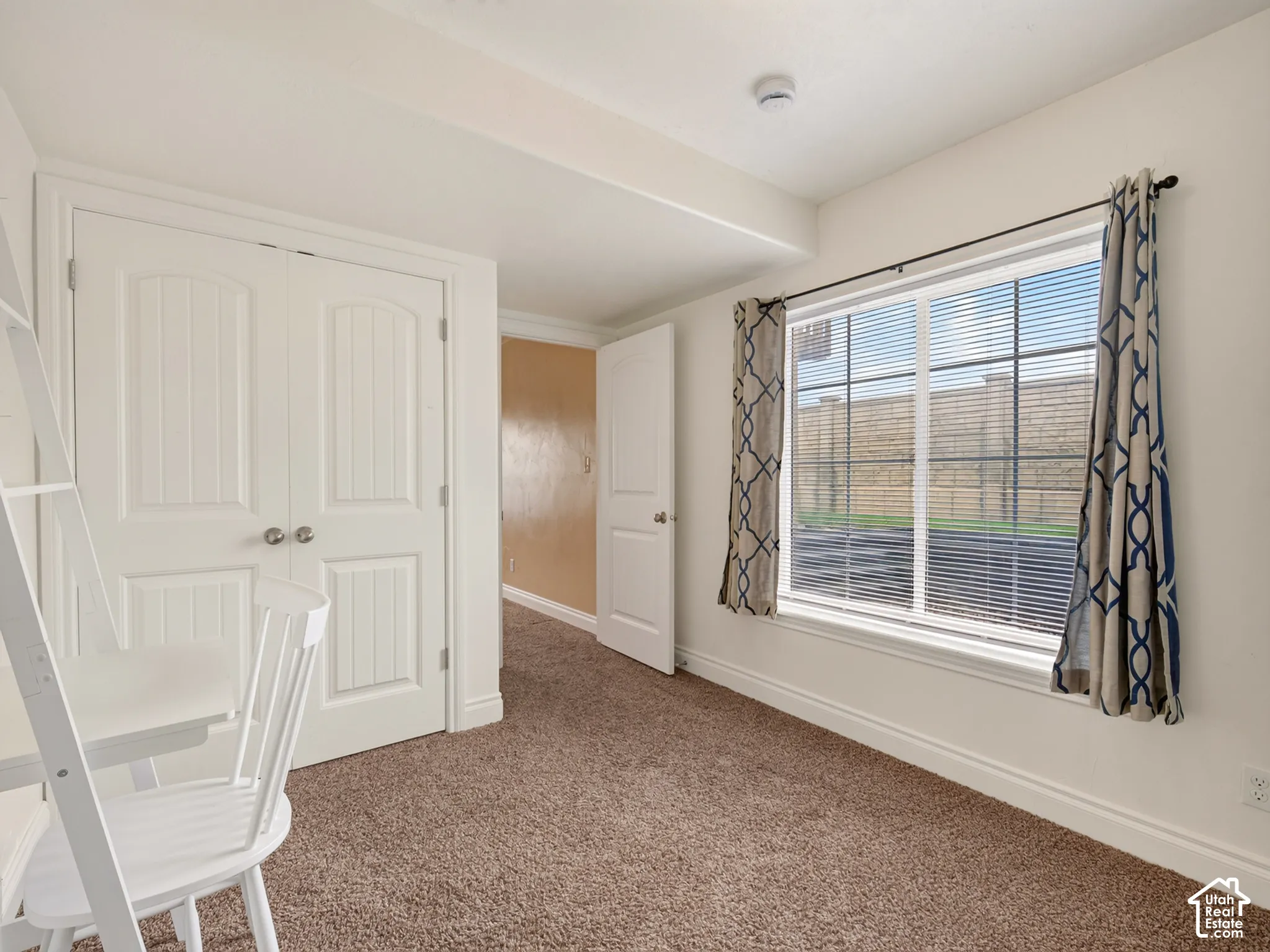 Room featuring neutral-toned carpeting, double-door closet with paneled detailing, and a large window with white casing