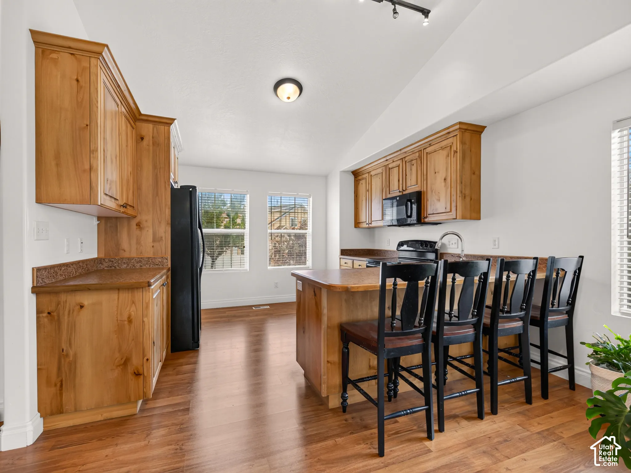 Kitchen featuring wood cabinetry, solid-surface countertops, wood-finish flooring, vaulted ceilings, and a center island with integrated seating