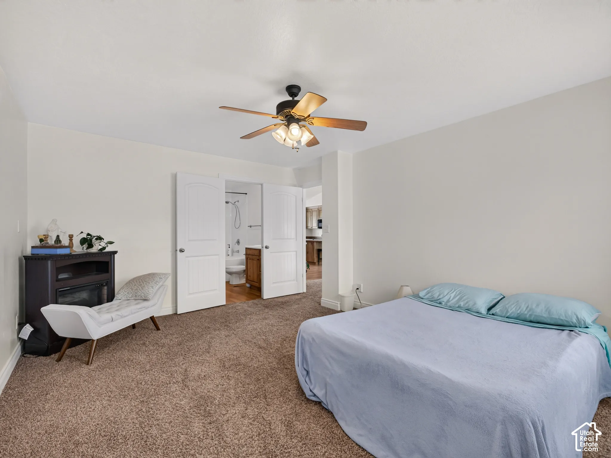 Neutral interior featuring wall-to-wall carpeting, a ceiling fan with integrated lighting, and double doors opening to a full bathroom