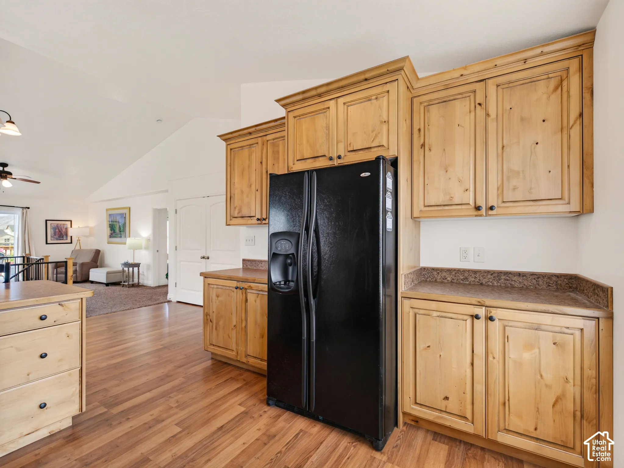 Kitchen featuring natural wood cabinetry, wood-finish flooring, stone-textured countertops, and a black side-by-side refrigerator