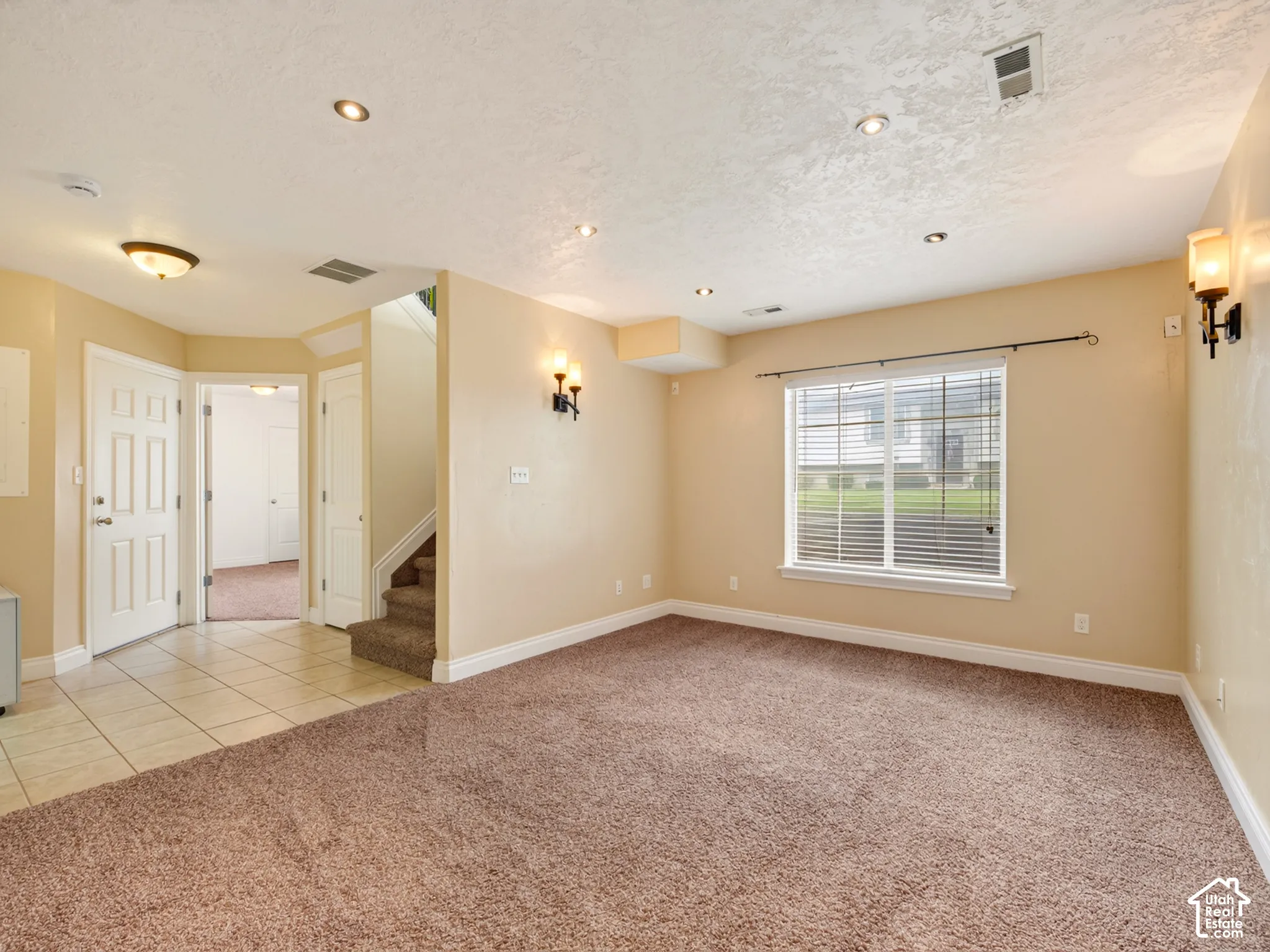 Interior space featuring neutral-tone wall finishes, recessed ceiling lighting, wall-mounted sconces, carpeted flooring, and ceramic tile flooring in the entry area
