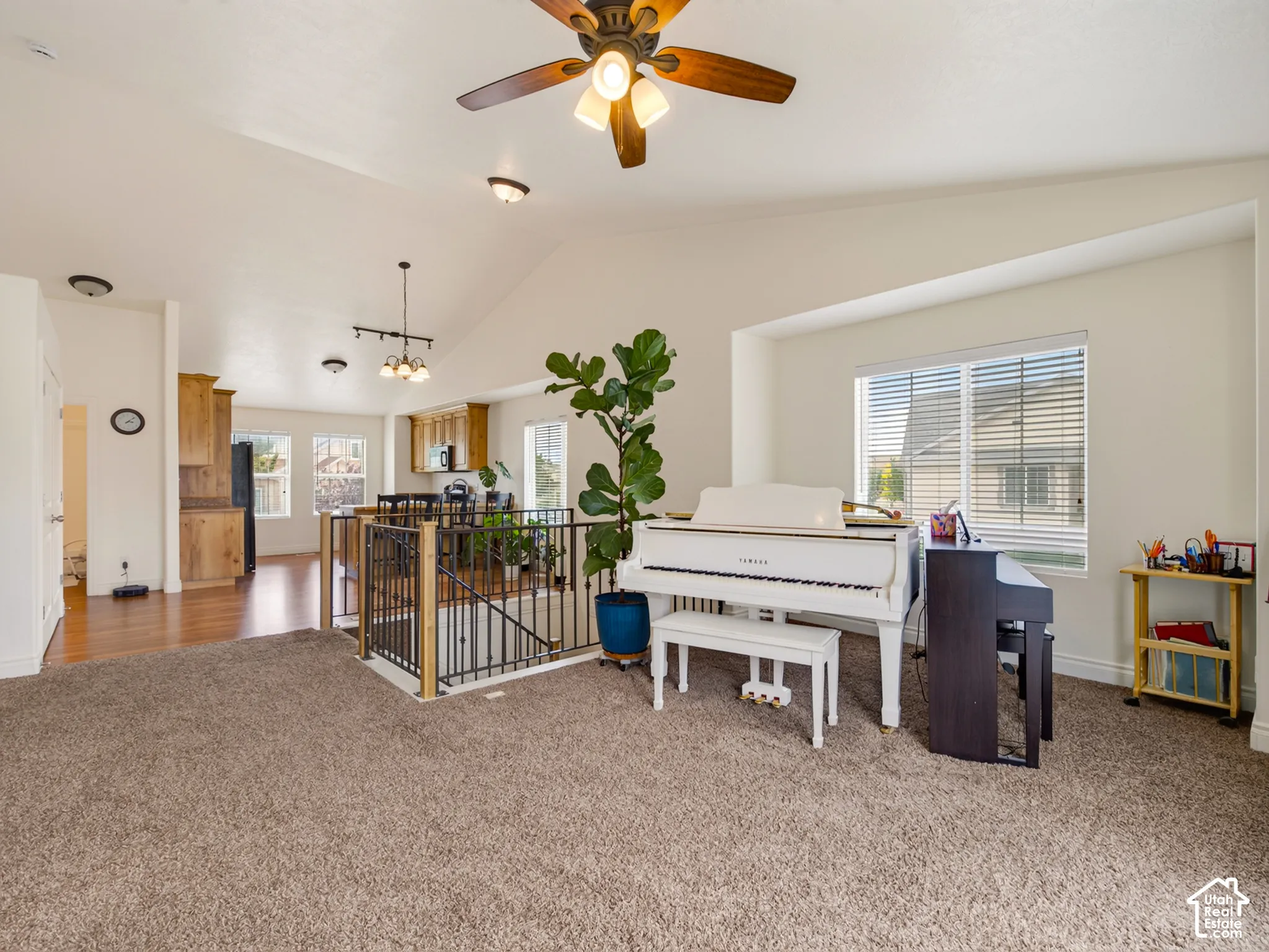 Vaulted ceilings, metal baluster staircase railing, wood-finish cabinetry, and multi-light ceiling fan