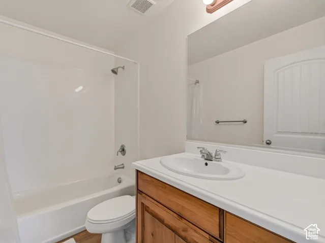Bathroom featuring a wood-finish vanity with a white countertop and oval undermount sink, a full-width wall mirror, and a tub-shower combination with white surround
