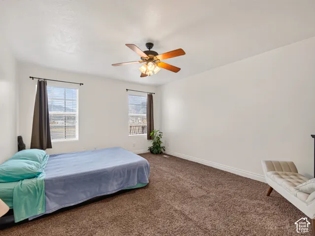 Spacious room featuring carpeting, two windows with grid patterns, and a ceiling fan with integrated lighting