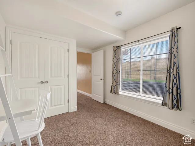 Room featuring neutral-toned carpeting, double-door closet with paneled detailing, and a large window with white casing