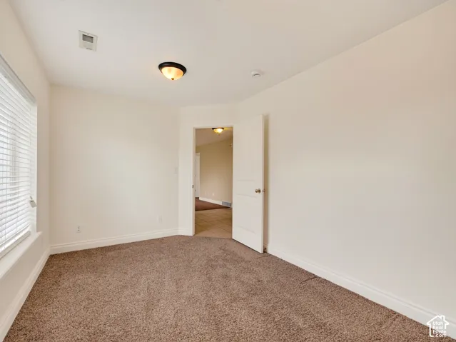 Neutral-toned room featuring neutral carpeting, a multi-panel interior door, and horizontal window blinds