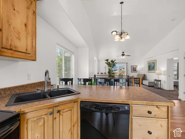 Kitchen featuring natural finish wood cabinetry, a dual-basin composite sink, integrated dishwasher, and a vaulted ceiling