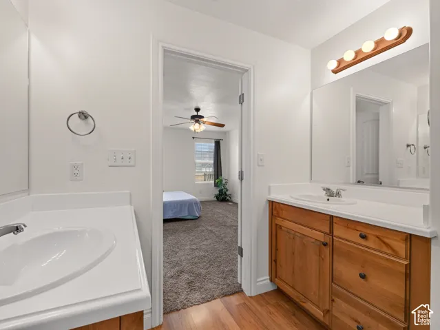 Dual-sink bathroom featuring wood-finish cabinetry, solid-surface integrated countertops, a full-width wall mirror, and overhead vanity lighting