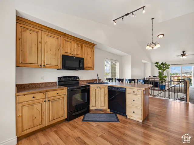 Kitchen featuring stained wood cabinetry, stone-finish countertops, black built-in appliances, vaulted ceilings, and wood-finish flooring