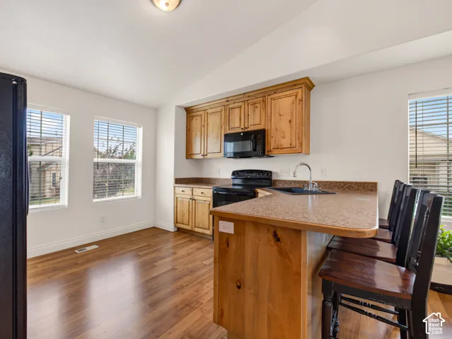 Kitchen featuring wood cabinetry, solid-surface countertops, wood-finish flooring, vaulted ceilings, and a breakfast bar