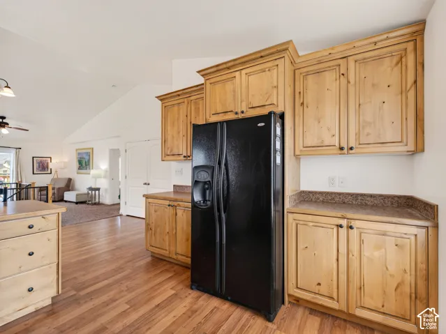 Kitchen featuring natural wood cabinetry, wood-finish flooring, stone-textured countertops, and a black side-by-side refrigerator